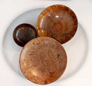 Three handcrafted wooden bowls on white surface.